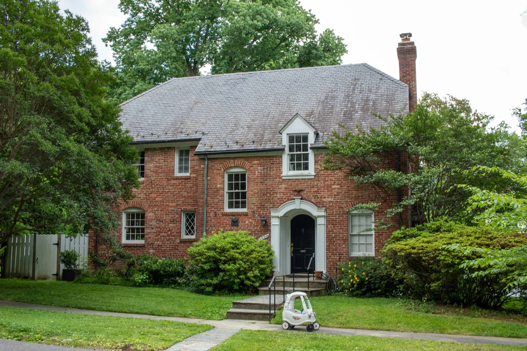 Brick colonial home with a slate roof and front garden