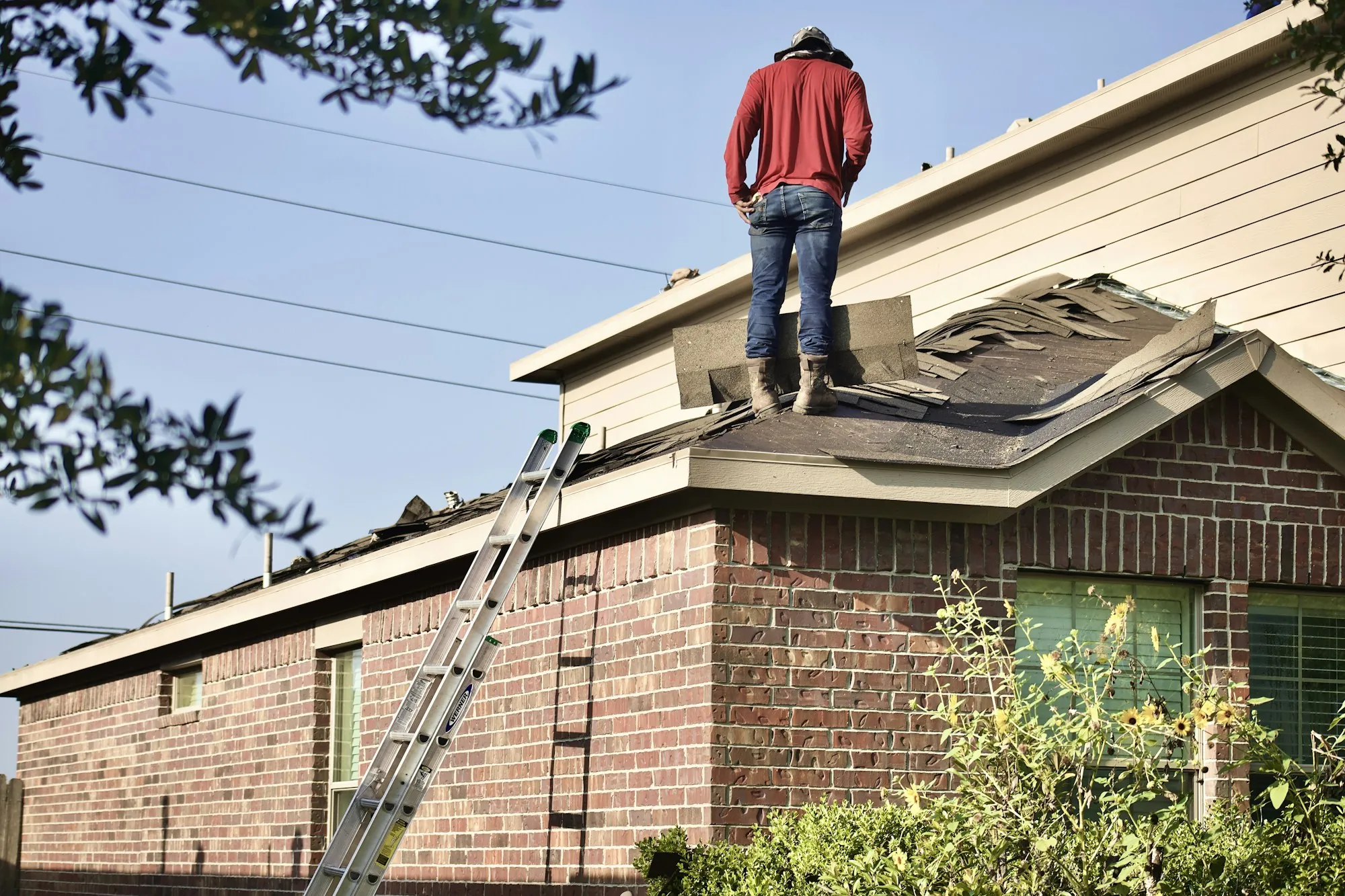Worker standing on the roof of a brick house with a ladder against the wall