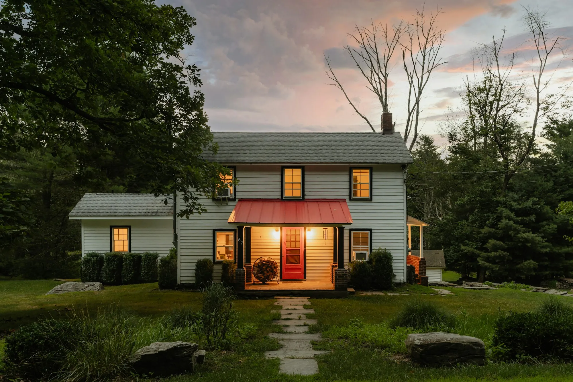 White two-story farmhouse with a glowing front porch at dusk